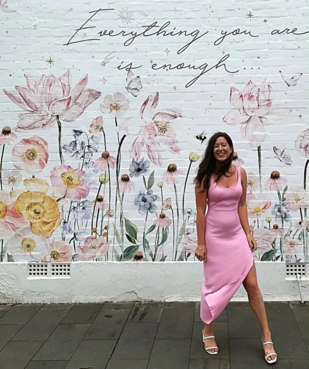 Lauren smiling in a pink dress in front of a flower mural